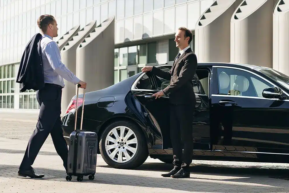 A premium chauffeur waiting at a Dubai hotel kerb with an executive sedan